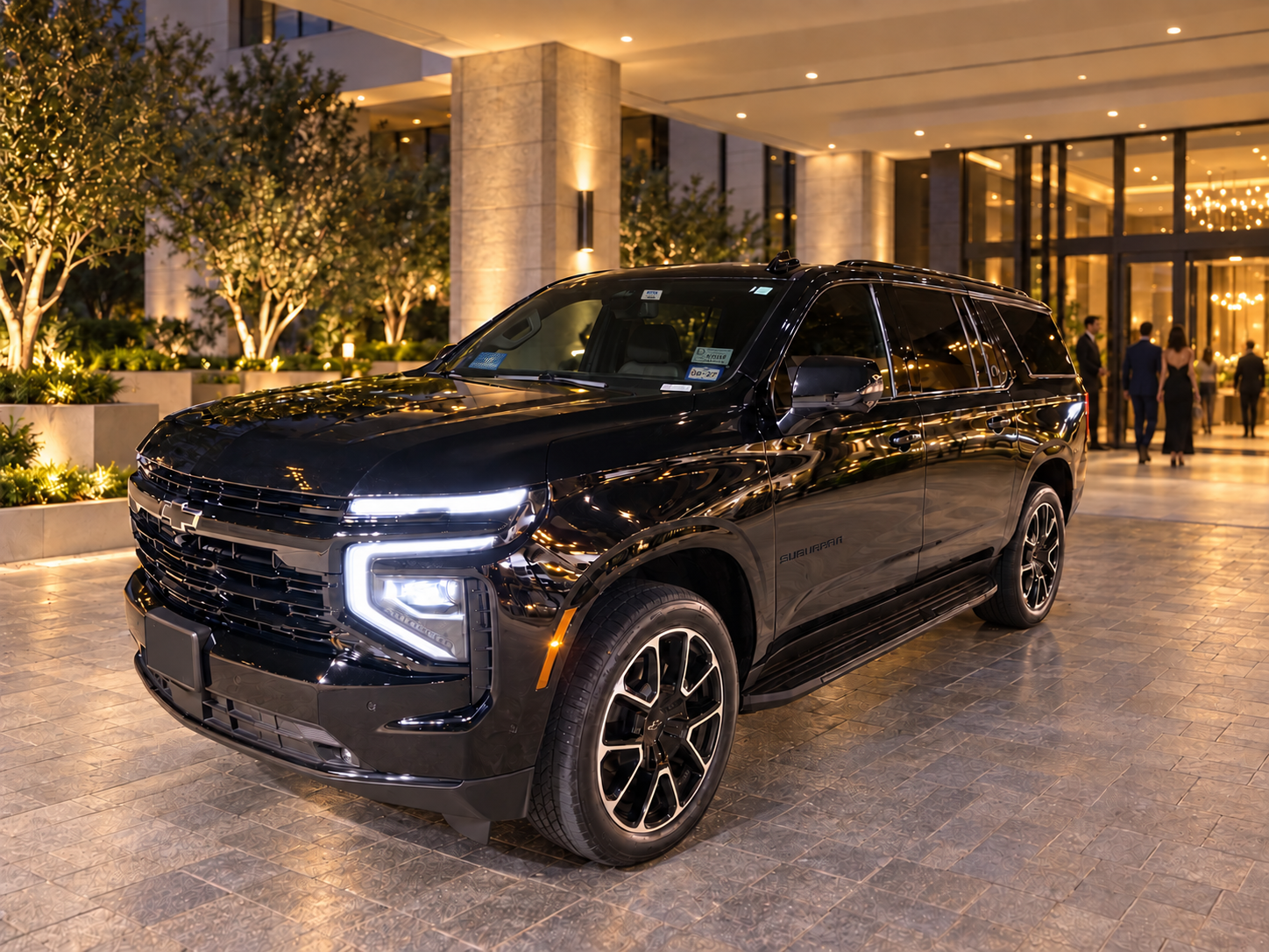 NoirRide black Chevrolet Suburban at an illuminated premium entrance as guests arrive